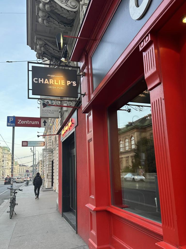 Der Eingang von "Charlie P's Irish Pub" in Wien mit einer markanten roten Fassade und einem schwarzen Schild mit weißer Schrift. Ein typischer Treffpunkt für Studenten und Besucher des Wiener Nachtlebens.