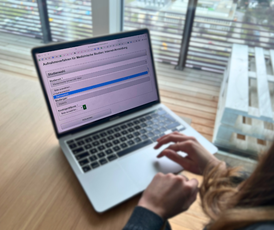Eine Person füllt online das Anmeldeformular für das Aufnahmeverfahren für medizinische Studien an einer Universität aus, mit einem Fokus auf der Auswahl des Studiengangs und des Studienjahres. Die Ansicht zeigt einen Laptop auf einem Tisch, im Hintergrund sind Fenster und ein urbaner Ausblick zu sehen.(Anmeldung zum MedAT)