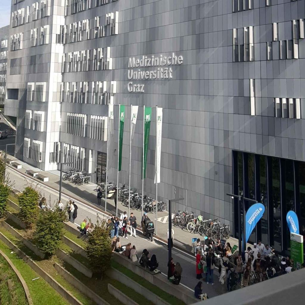 Foto des modernen Gebäudes der Medizinischen Universität Graz. Im Vordergrund sind viele Studierende und Besucher zu sehen, die sich für die MedAT-Zulassung und mögliche Studienwechsel informieren